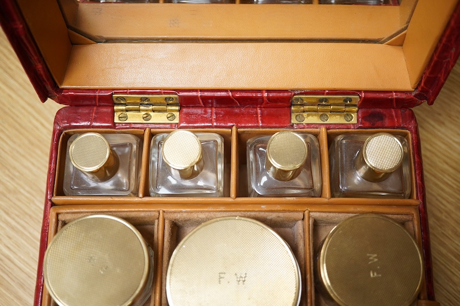 A red stained crocodile skin two layer vanity case, fitted with brass topped bottles and pots, case 22cm wide x 13.5cm high. Condition - handle has pulled away one side and needs re stitching